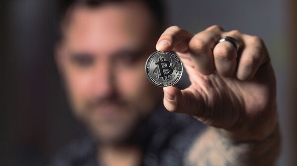Una persona con una moneda de bitcóin - Sputnik Mundo