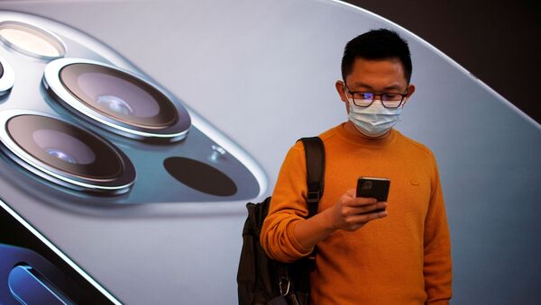 Un hombre chino con la imagen de un iPhone 12 detrás de él - Sputnik Mundo