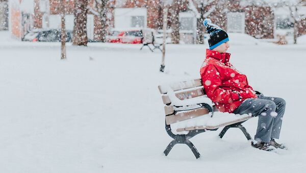 Una persona sentada en un banco durante una nevada - Sputnik Mundo