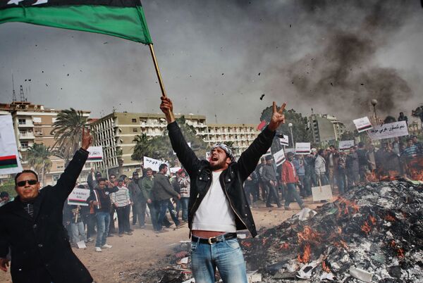 Desde Túnez, la ola de disturbios se extendió a Argelia, Jordania, Egipto y Yemen antes de llegar a otros países. En la foto: Residentes de Bengasi, Libia, queman retratos de Muammar Gaddafi, carteles con sus citas y el 'Libro Verde' - 2 de marzo de 2011. - Sputnik Mundo