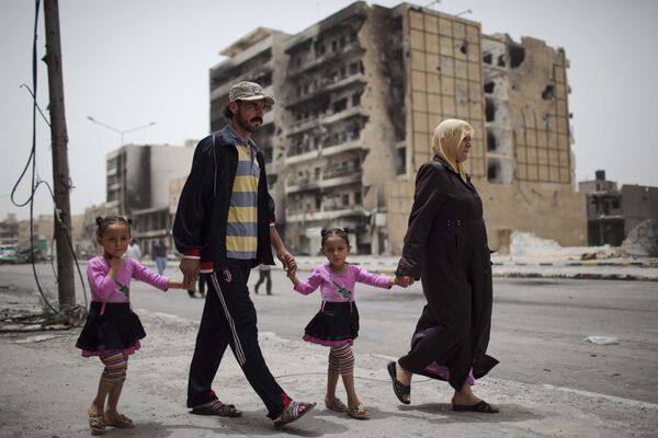 Libia, donde al menos 50.000 personas murieron durante la Primavera Árabe y la posterior intervención extranjera, sigue dividida, carece de un gobierno unificado y tiene tropas y mercenarios extranjeros en su territorio desde el asesinato de Gaddafi. En la foto: una familia en una calle de Trípoli - 22 de mayo de 2011. - Sputnik Mundo