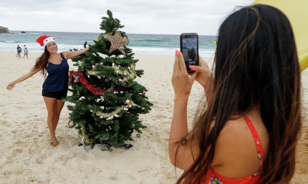 Una joven se toma fotos cerca de un árbol de Navidad en una playa de Sidney, Australia. - Sputnik Mundo