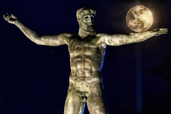 Esta imagen registrada el 29 de diciembre de 2020 muestra la Luna saliendo detrás de la escultura del dios del mar, Poseidón, en Corinto (Grecia). - Sputnik Mundo
