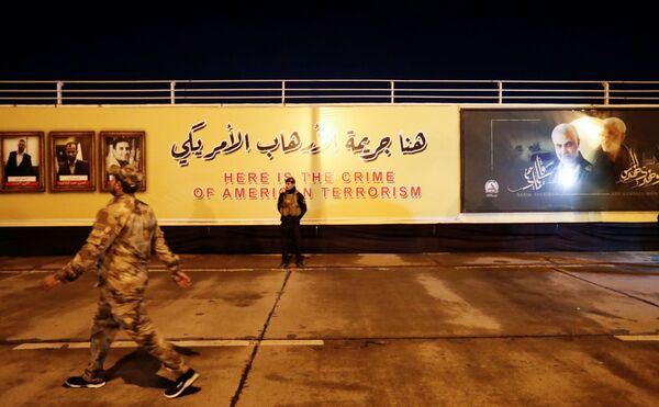 Un miembro de la las Fuerzas de Movilización Popular (PMF) delante de un mensaje que dice: Aquí está el crimen del terrorismo estadounidense, en el aeropuerto internacional de Bagdad. - Sputnik Mundo