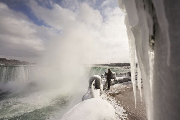 Una mujer se acerca a un mirador cubierto de hielo para tomar una foto de las cataratas en Ontario, Canadá. - Sputnik Mundo