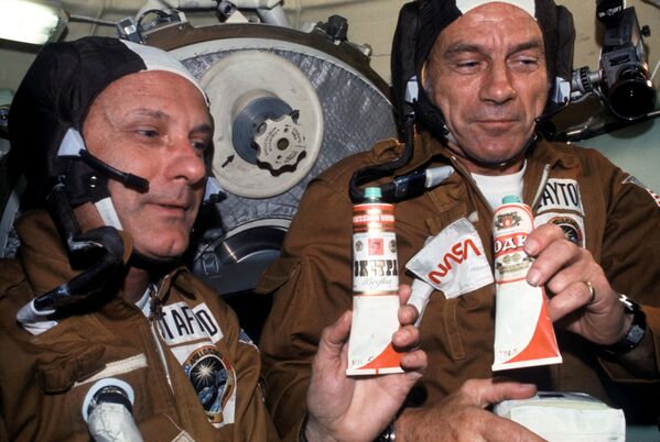 Astronautas Thomas P. Stafford y Donald K. &#x27;Deke&#x27; Slayton con bolsas de alimentos espaciales soviéticos en el módulo orbital Soyuz durante la misión conjunta de acoplamiento en órbita terrestre del Proyecto de Prueba Apolo-Soyuz de EEUU y la URSS. En los tubos se lee &#x27;vodka&#x27; aunque son etiquetas falsas pegadas de broma para brindar. De hecho, dentro de los tubos hay borsch, una sopa tradicional de remolacha.  - Sputnik Mundo