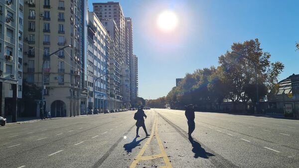 Dos personas cruzan una calle casi desierta Buenos Aires durante el feriado del 25 de mayo - Sputnik Mundo