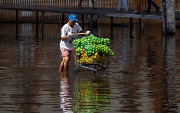 Un hombre lleva un carrito de frutas a lo largo de una calle inundada en el centro de Manaus (Brasil). - Sputnik Mundo