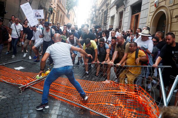Unos manifestantes remueven una barrera instalada por la policía para bloquear su paso mientras marchan en contra del Green Pass, una especie de pasaporte COVID-19 que será obligatorio para cenas en interiores, eventos culturales y deportivos a partir de la próxima semana, en Roma (Italia). - Sputnik Mundo