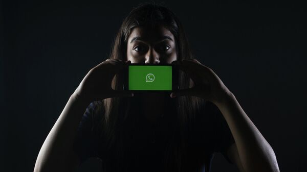 Una persona sostiene un móvil con el logotipo de WhatsApp - Sputnik Mundo