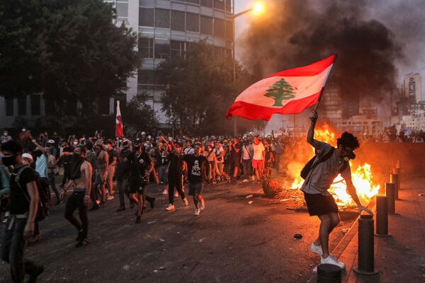 Hace un año ocurrió la explosión que asoló el puerto más importante del Líbano, ubicado en la ciudad de Beirut, y, para conmemorarlo, cientos de libaneses salieron a las calles a protestar por la impunidad de la peor catástrofe que sufrió el país en tiempos de paz y en un momento en que su economía sufría por la crisis económica. En la foto: un manifestante con una bandera nacional libanesa durante los enfrentamientos en la protesta. - Sputnik Mundo