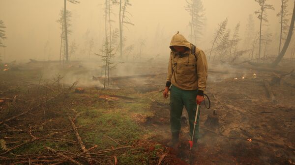 Un especialista del servicio local de protección forestal extingue un incendio forestal cerca del pueblo de Magaras en la región de Yakutia, Rusia, el 17 de julio de 2021 - Sputnik Mundo