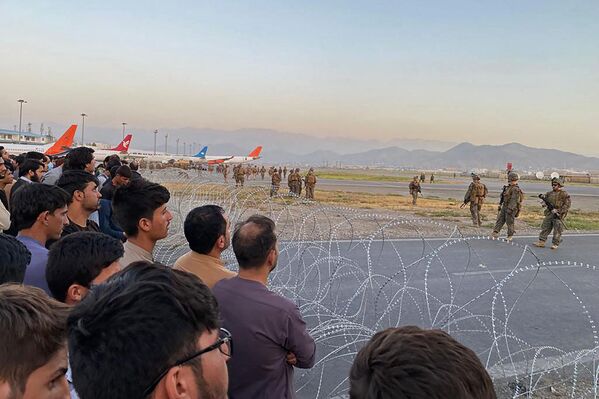 El Departamento de Defensa de EEUU ha ordenado el envío de 1.000 soldados adicionales a Kabul para ayudar a evacuar a los ciudadanos estadounidenses. En la foto: los residentes afganos observan a varios soldados estadounidenses detrás de un alambrado de seguridad que les impide la entrada. - Sputnik Mundo