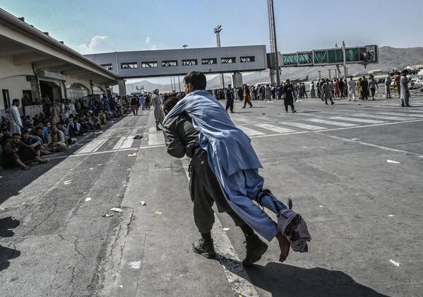 Un voluntario transporta a un hombre herido mientras otras personas esperan en el aeropuerto de Kabul el 16 de agosto de 2021. Un voluntario transporta a un hombre herido mientras otras personas esperan en el aeropuerto de Kabul el 16 de agosto de 2021. - Sputnik Mundo