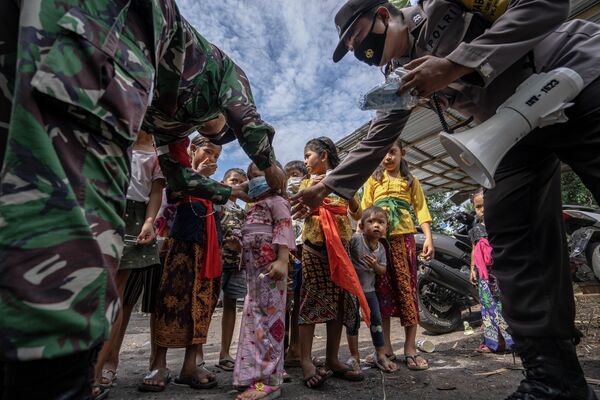 Esta impresionante imagen que muestra a los miembros de la Guardia Nacional y la Policía de la isla de Bali repartiendo mascarillas entre los niños, captada por Edy Gautama, ocupó el tercer lugar en la categoría Los héroes de la pandemia. El fotógrafo la tituló Guardian Angel (Un ángel de la guarda). - Sputnik Mundo