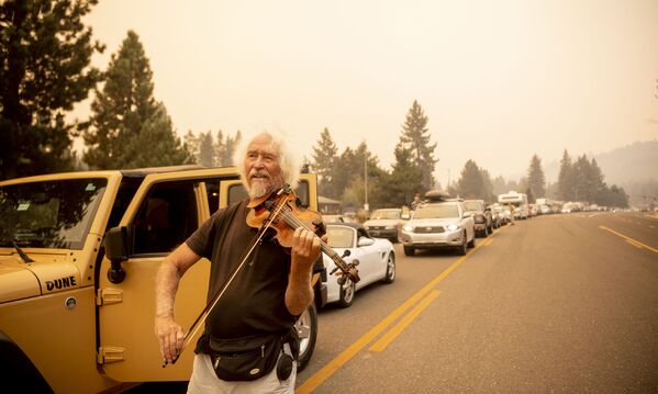 Mel Smothers toca el violín mientras permanece atrapado en el tráfico con los evacuados a medida que los vecinos intentan huir del incendio Caldor en el lago Tahoe, California, el 30 de agosto de 2021. Se han quemado al menos 650 estructuras y miles más están amenazadas a medida que el fuego avanza hacia la zona turística. - Sputnik Mundo