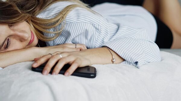Una persona en la cama con un teléfono en la mano - Sputnik Mundo