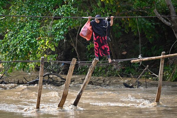 Una mujer cruza el río en un puente destruido por las inundaciones del año pasado en la Provincia de Célebes Meridional (Indonesia). - Sputnik Mundo