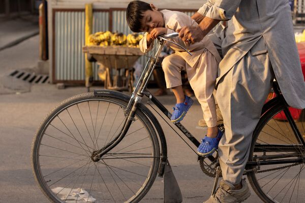 Un padre y su hijo dormido van en bicicleta por una calle de Kabul, Afganistán. - Sputnik Mundo