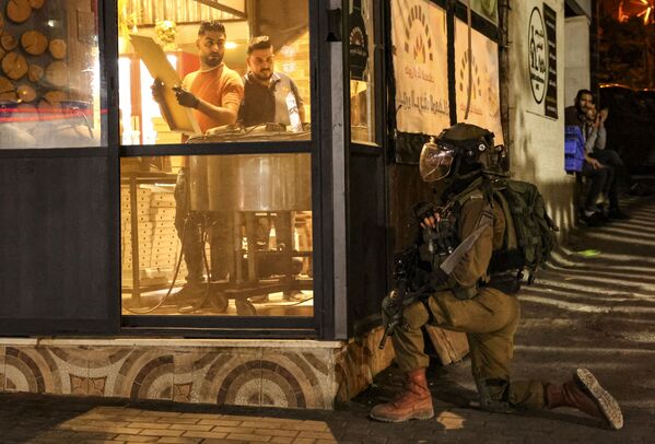 Los empleados de una panadería miran fijamente a un miembro de las Fuerzas de Seguridad israelíes mientras toma posición en la esquina de una calle, durante los enfrentamientos con los palestinos que protestan en Hebrón, una ciudad palestina situada en Cisjordania, en solidaridad con los prisioneros detenidos en las cárceles israelíes, el 5 de noviembre de 2021. - Sputnik Mundo