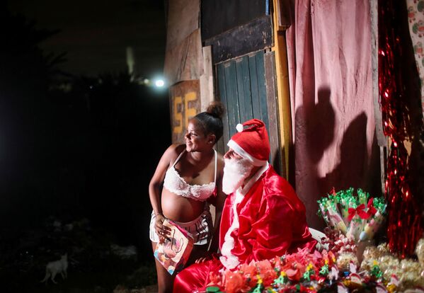 Un hombre disfrazado de Papá Noel reparte regalos donados a niños de la favela de Cidade de Deus —ciudad de dios—.En la foto: la entrega de un regalo a Caroline Vitoria, una niña embarazada de 16 años. - Sputnik Mundo