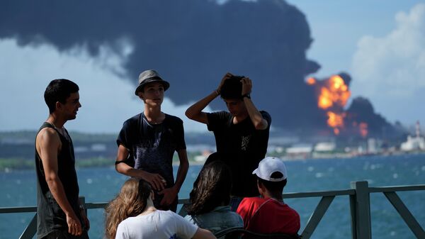 Jóvenes cubanos en el muelle del puerto de Matanzas frente a un tanque de almacenamiento de petróleo en llamas.  - Sputnik Mundo