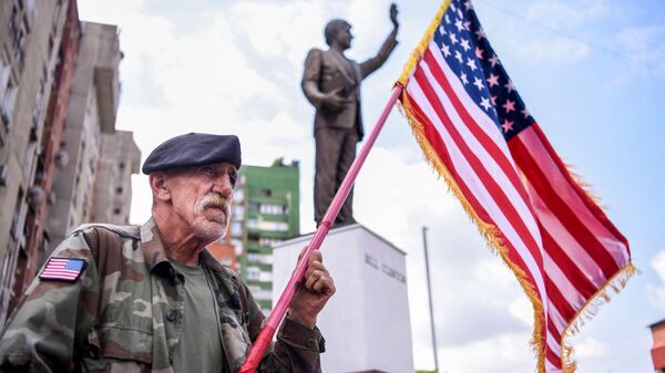 Un hombre kosovar de origen albanés sostiene una bandera de EEUU frente a una estatua de Bill Clinton - Sputnik Mundo