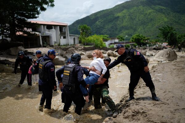 Agentes de policía llevan a una mujer al otro lado de una calle inundada en El Castaño, Venezuela, donde tres personas murieron por el temporal. - Sputnik Mundo