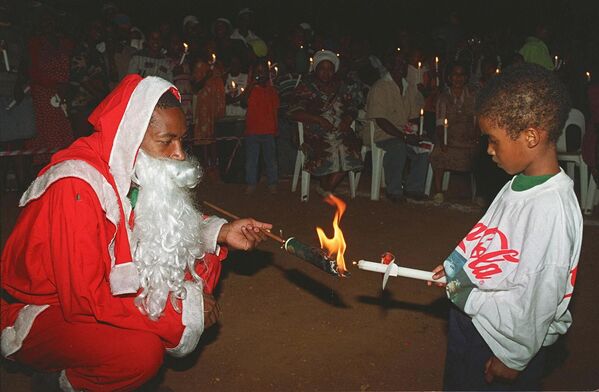 Father Christmas ayuda a encender la vela de Navidad a un niño en Soweto, una zona de población predominantemente africana de Johannesburgo (Sudáfrica). - Sputnik Mundo