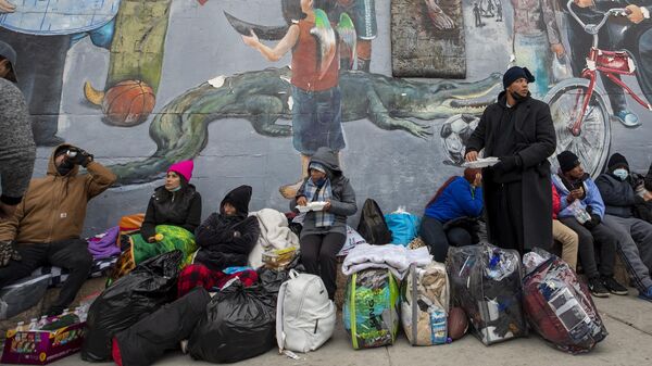 Migrantes comen y esperan ayuda mientras acampan en una calle del centro de El Paso, Texas, el domingo 18 de diciembre de 2022.   - Sputnik Mundo