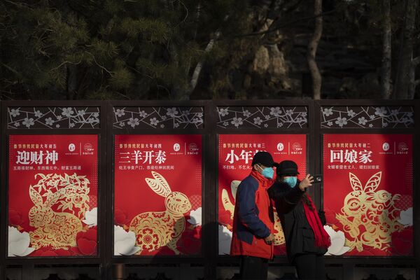 Unos visitantes con máscaras posan frente a una hilera de vallas publicitarias temáticas del Año del Conejo en un parque público de Pekín. - Sputnik Mundo