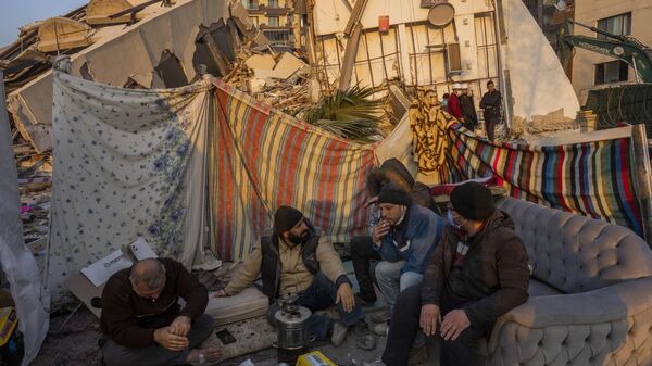 Hombres sentados frente a los escombros de una zona destruida durante el terremoto en Antakya, sureste de Turquía, el 12 de febrero de 2023 - Sputnik Mundo