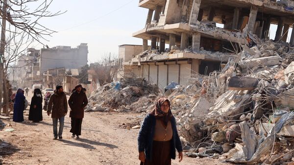 Residentes caminan junto a edificios destruidos, mientras continúan las operaciones de búsqueda y rescate días después de que un mortífero terremoto  en la ciudad de Jindayris, en la parte de la provincia siria de Alepo, el 10 de febrero de 2023 - Sputnik Mundo