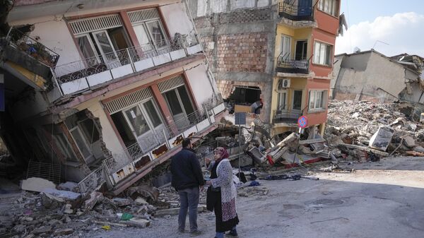 Dos personas conversan en medio de edificios dañados en Hatay, Turquía, el sábado 11 de febrero de 2023. - Sputnik Mundo