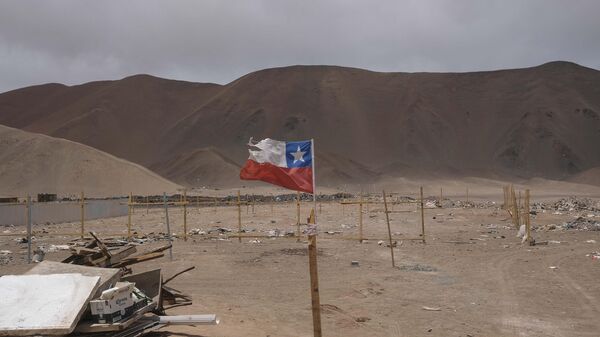 Una bandera chilena ondea en un poste de madera en un terreno donde se concentran los migrantes en Chile. - Sputnik Mundo