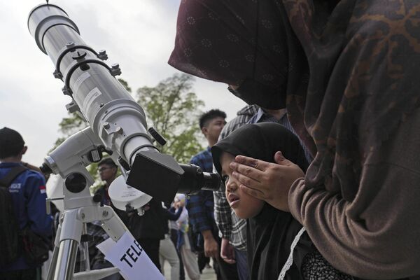 El eclipse duró hasta las 6:59:14 (hora UTC).  En la foto: una madre ayuda a su hija a ver a través de un telescopio para observar el eclipse solar híbrido en Yakarta, Indonesia. - Sputnik Mundo