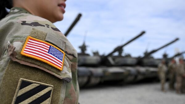 Una insignia de la bandera estadounidense se ve en el uniforme de una soldado estadounidense mientras se encuentra cerca de tanques en la base de entrenamiento militar del Ejército de Estados Unidos - Sputnik Mundo