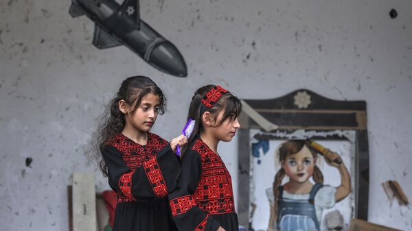 Una niña palestina cepilla el pelo de otra delante de un mural durante una exposición titulada 'La ocupación mata a la infancia' en Gaza, Palestina. - Sputnik Mundo