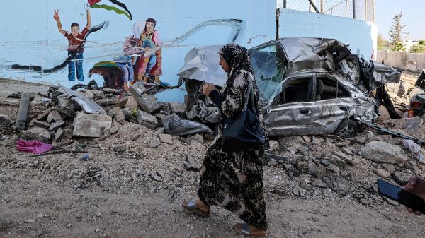 Una mujer pasa junto a los restos de un coche en una calle de la ciudad ocupada de Yenín, en Cisjordania, el 5 de julio de 2023, después de que el Ejército israelí declarara el fin de una operación militar de dos días en la zona.  - Sputnik Mundo