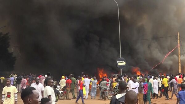 Con la sede del partido gobernante ardiendo por la espalda, partidarios de los soldados amotinados se manifiestan en Niamey, Níger, el jueves 27 de julio de 2023. - Sputnik Mundo