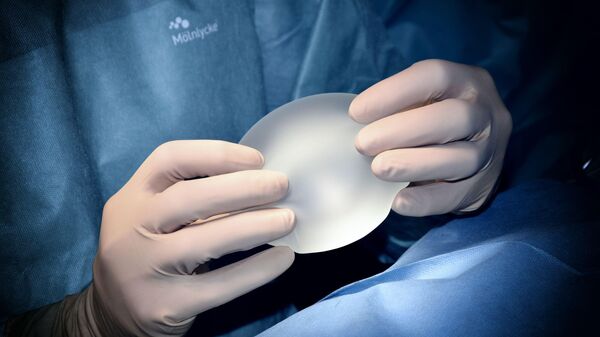 Un cirujano con un implante mamario en las manos durante una cirugía estética - Sputnik Mundo