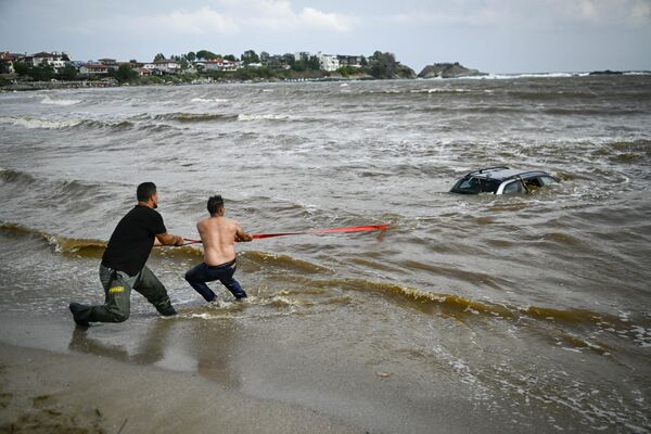 Varias personas intentan sacar un coche sumergido en la costa búlgara del mar Negro. - Sputnik Mundo
