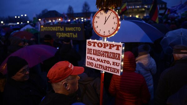 Un hombre sostiene una pancarta con la leyenda Detengan a los belicistas EEUU, la OTAN y la UE durante un mitin de Alternativa para Alemania (AfD), el 24 de febrero de 2023. - Sputnik Mundo
