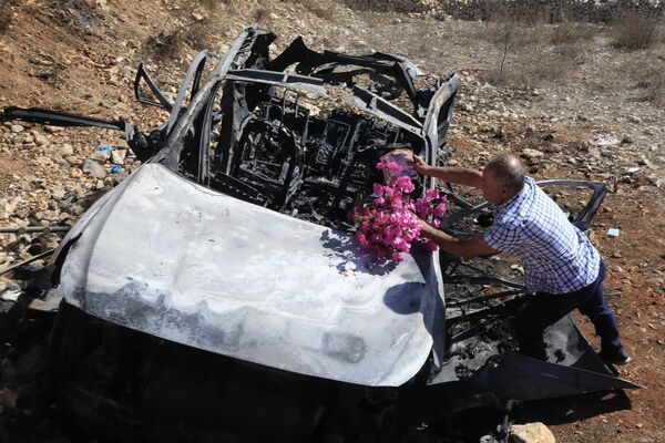 Un libanés deposita flores sobre los restos quemados de un automóvil en el que murieron sus familiares durante el bombardeo israelí al sur del Líbano. - Sputnik Mundo