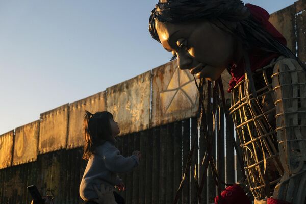 Una niña observa a la Pequeña Amal, una muñeca gigante de más de 3,5 metros de altura que representa a una migrante siria de 10 años, en Playas de Tijuana, en la frontera entre México y EEUU. La muñeca, que actualmente se encuentra en México, está recorriendo el mundo para concienciar sobre el problema de los refugiados. - Sputnik Mundo