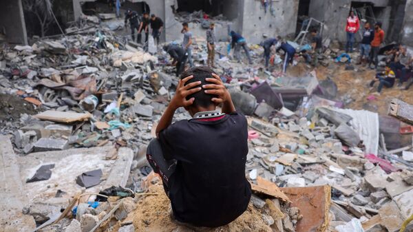 Un niño reacciona mientras la gente rescata pertenencias entre los escombros de un edificio dañado tras los ataques contra Rafah, en el sur de la Franja de Gaza, el 12 de noviembre de 2023 - Sputnik Mundo