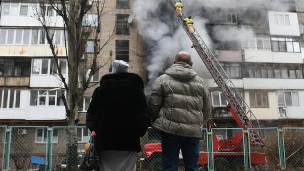 Personas observan cómo bomberos extinguen un incendio en un edificio residencial de Donetsk, provocado por bombardeos de Ucrania - Sputnik Mundo