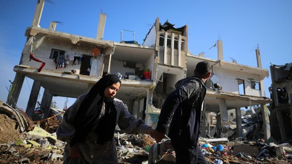 Palestinos caminan junto a un edificio destruido en el campo de refugiados de al-Maghazi, en el centro de la Franja de Gaza - Sputnik Mundo