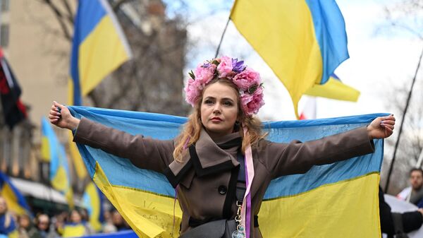 Una manifestante sostiene una bandera ucraniana, el 25 de febrero de 2023  - Sputnik Mundo