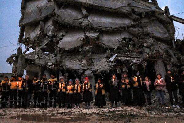 El 6 de febrero de 2023, dos potentes terremotos, con solo nueve horas de diferencia, destruyeron 160.000 edificios en Turquía y Siria. En la foto: miembros de la Defensa Civil Siria y supervivientes locales del devastador sismo del año pasado asisten a una vigilia conmemorativa en la ciudad de Jindairis, en la provincia noroccidental siria de Alepo. - Sputnik Mundo
